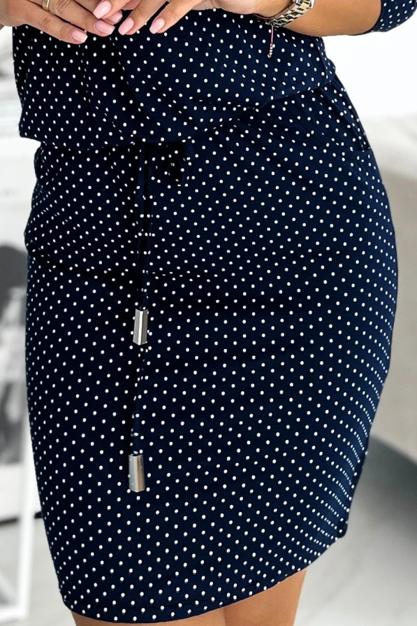 Tumši zila sportiska kleita ar baltu punktu rakstu un regulējamu auklu jostasvietā. Kleita ir izgatavota no elastīga materiāla, kas nodrošina komfortu un eleganci ikdienas valkāšanai.