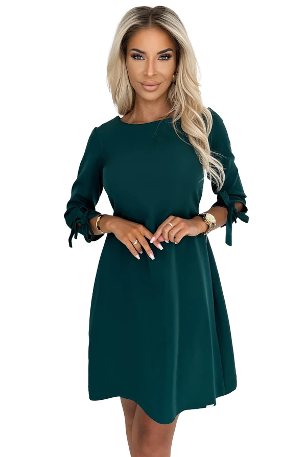 Zaļā trapezveida kleita ar trīs ceturtdaļu piedurknēm un dekoratīvām saitēm. Elegants un vienkāršs dizains, kas piemērots dažādiem gadījumiem.