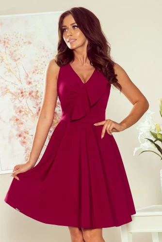 Sieviešu kleita košā bordo krāsā ar elegantu volānu pie kakla izgriezuma. Kleita ir bez piedurknēm un ar viegli izplestu svārku daļu, kas piešķir tai sievišķīgu šarmu.}