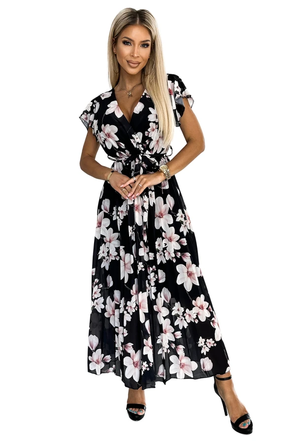 Garā, melnā kleita ar ziedu rakstu un plisētu audumu, kas piešķir eleganci un kustību. Kleitai ir īsas piedurknes un josta, kas izceļ vidukli.