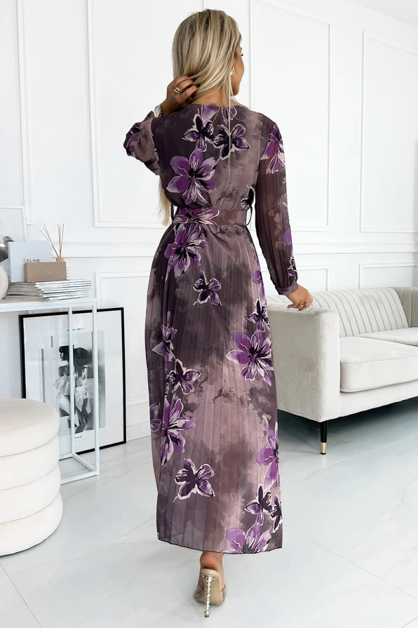 Sieviete valkā garu, plīvojošu kleitu ar violetiem ziedu rakstiem uz šifona auduma. Kleita ir eleganta un piemērota gan ikdienas, gan svinīgiem pasākumiem.